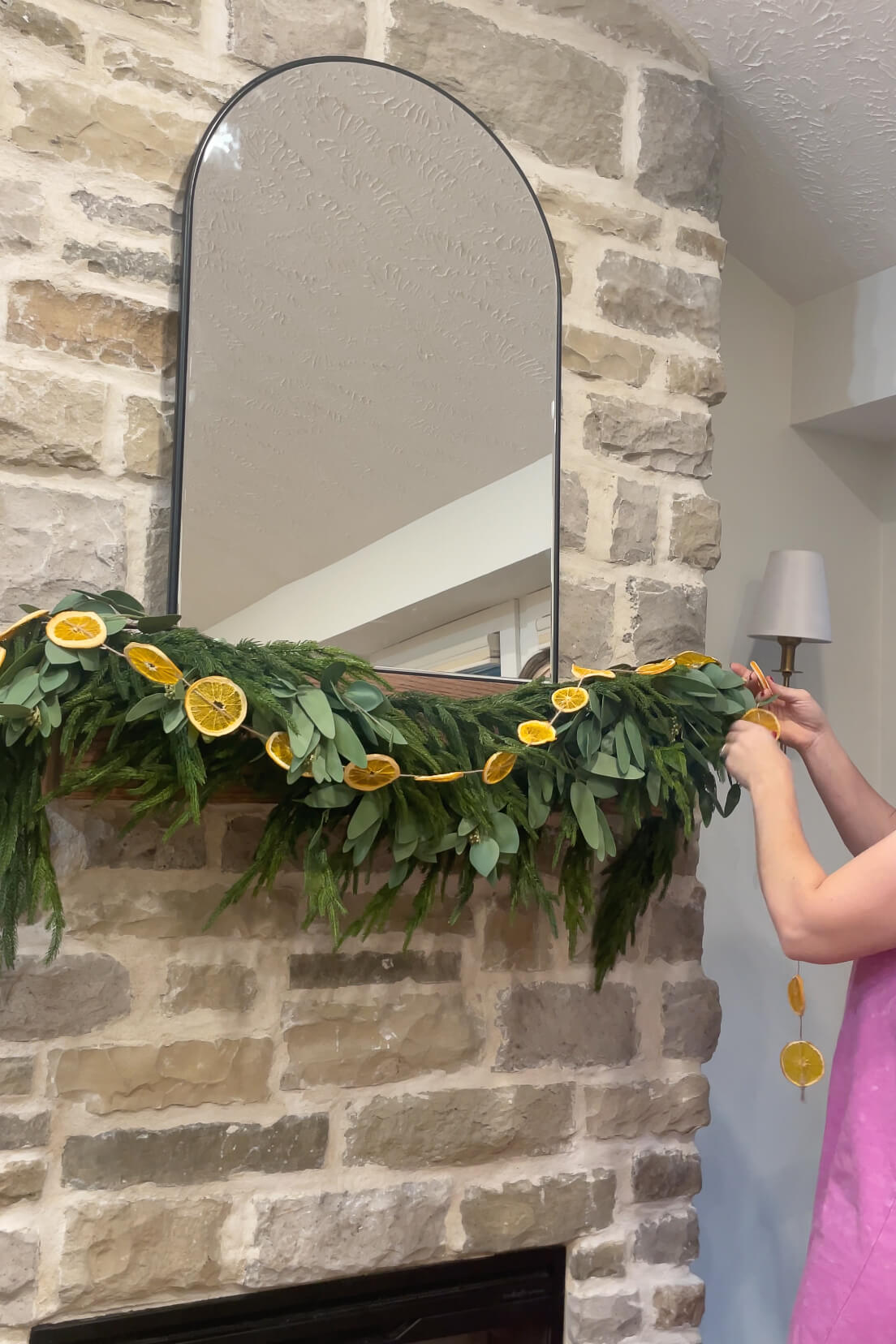 hanging a homemade dried orange slice garland on a fireplace mantel for Christmas decor.